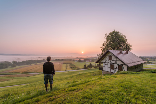 Man posing in front of beautiful sunrise by the medieval house in rural countryside of Slovenia